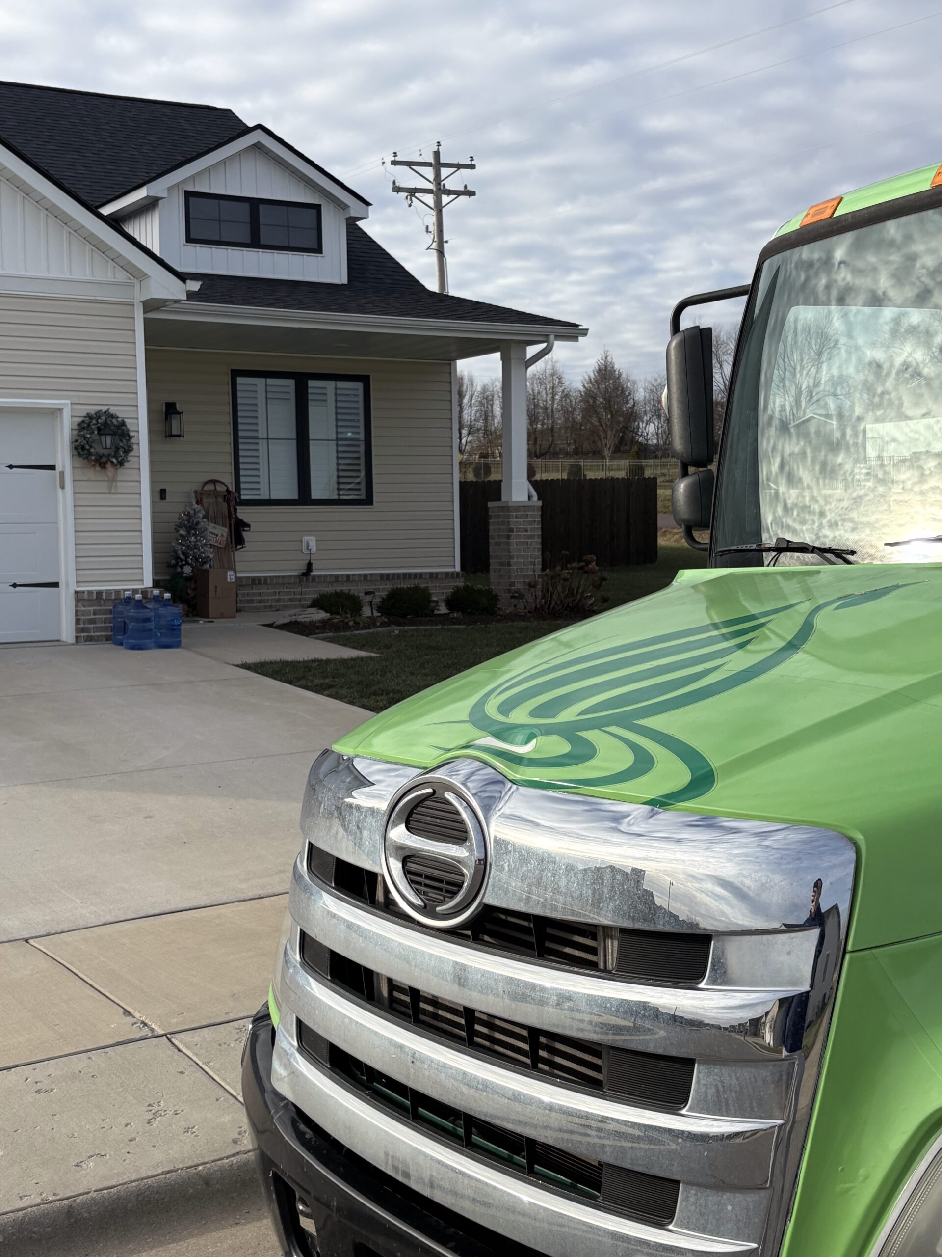 Close-up of green truck grill with suburban home behind.